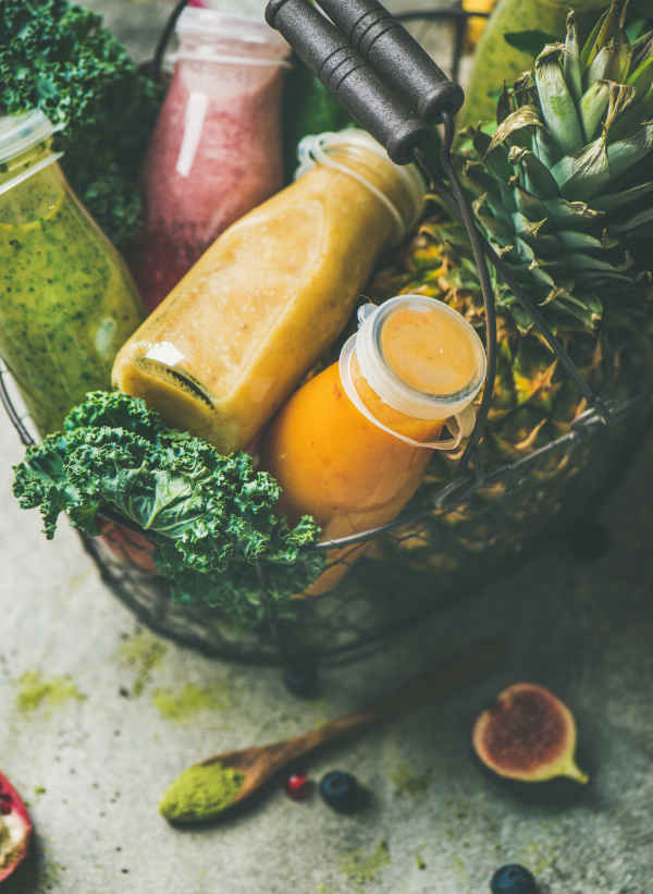 Colorful smoothies in bottles with fruits in basket, grey background
